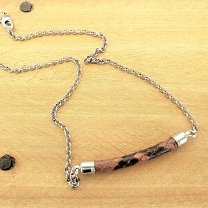 May include: A silver chain necklace with a brown and black patterned leather bar pendant.