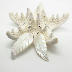 May include: A pair of white mother of pearl leaf earrings with silver hooks. The earrings are displayed on a white starfish.