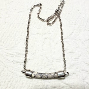May include: A silver chain necklace with a white and gray snake skin bar pendant.