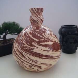 May include: A brown and white ceramic vase with a swirling marbled pattern. The vase has a round body and a narrow neck.