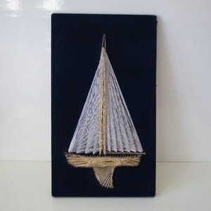 Peut inclure: Un voilier blanc avec des accents dorés est encordé avec du fil sur un fond bleu foncé.