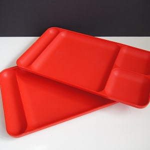 May include: Two red plastic serving trays with divided sections. The top tray has three sections, and the bottom tray has one large section.