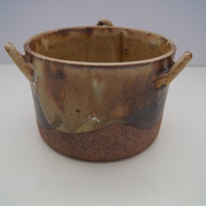 May include: A brown and tan ceramic bowl with two handles. The bowl has a speckled glaze and a rough texture.