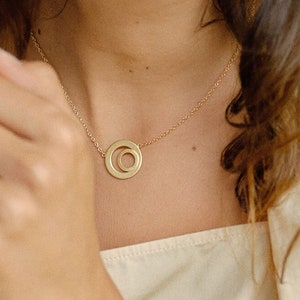 Könnte beinhalten: Eine goldene Halskette und ein Armband mit einem Doppelkreis-Anhänger. Halskette und Armband sind beide zart und schlicht.