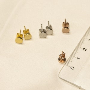 May include: A set of four stud earrings in gold, silver, and rose gold. The earrings are small and round, and they are arranged in a row on a white surface.
