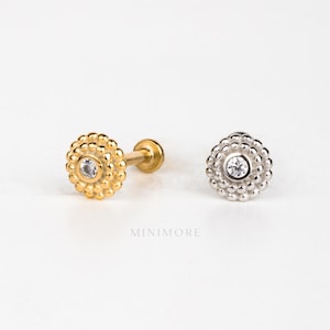 May include: Two small stud earrings, one gold-toned and one silver-toned. Each earring has a central clear stone surrounded by a beaded, circular design. The earrings are presented on a white background.