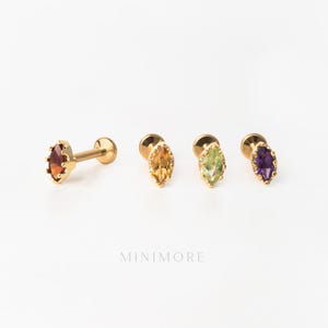 Pode incluir: Quatro brincos de pino dourados com pedras preciosas de corte marquise em vermelho, amarelo, verde e roxo. Cada brinco possui uma parte traseira circular plana e um pino. O texto MINIMORE está impresso em letras cinzas sob as peças.