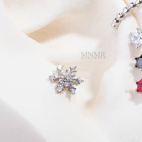 May include: A close-up of a silver snowflake earring with clear cubic zirconia stones. The earring is on a white background. The text "MNMR minimore" is visible in the image.