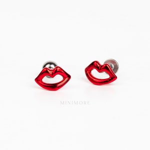 May include: A pair of red lip-shaped earrings with silver posts. The earrings are made of metal and have a shiny finish.