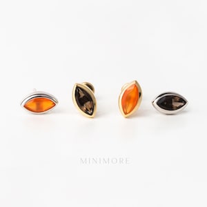 May include: Four marquise-shaped stud earrings arranged in a row. Two earrings feature vibrant orange stones set in silver-toned metal, while the other two feature dark, translucent smoky stones set in gold-toned metal. The text MINIMORE is visible.