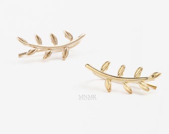 May include: A pair of gold-toned ear climbers shaped like delicate branches with small leaves. Each earring features a curved stem with four distinct leaf-like segments extending outward. The text MNMR minimore is printed in small letters.