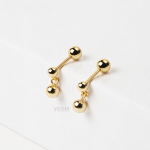 May include: A pair of gold dangle earrings with two small round balls on each earring.