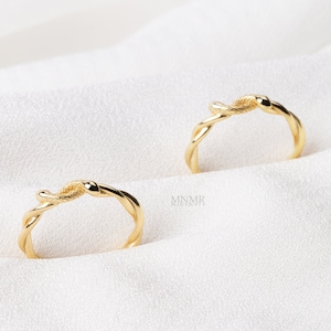 May include: Two gold-toned rings with a snake design. The rings are intertwined and have a smooth, polished finish.