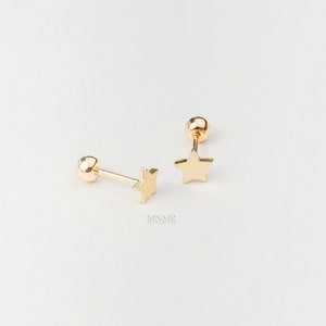 Peut inclure: Une paire de boucles d'oreilles clous en forme d'étoile dorées. Chaque boucle d'oreille présente un petit charme en forme d'étoile à cinq branches attaché à une tige avec une boule dorée à l'extrémité.