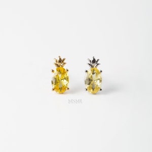 May include: Two pineapple-shaped stud earrings. One is gold-toned with a yellow oval-cut stone, the other is silver-toned with a yellow oval-cut stone. The earrings have a crown-like top and are set against a white background.