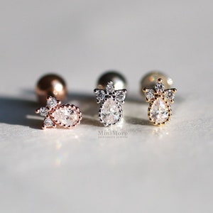 Puede incluir: Tres pendientes en forma de lágrima con una piedra transparente y un halo de piedras más pequeñas. Los pendientes están disponibles en oro rosa, plata y oro.