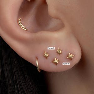 May include: Close-up of an ear adorned with gold earrings. The ear features a crescent moon stud, a small hoop, and several star-shaped studs. The studs are labeled "Type A" and "Type B".