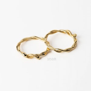 May include: Two gold-toned rings with a twisted, vine-like design. The rings are intertwined and appear to be made of metal.