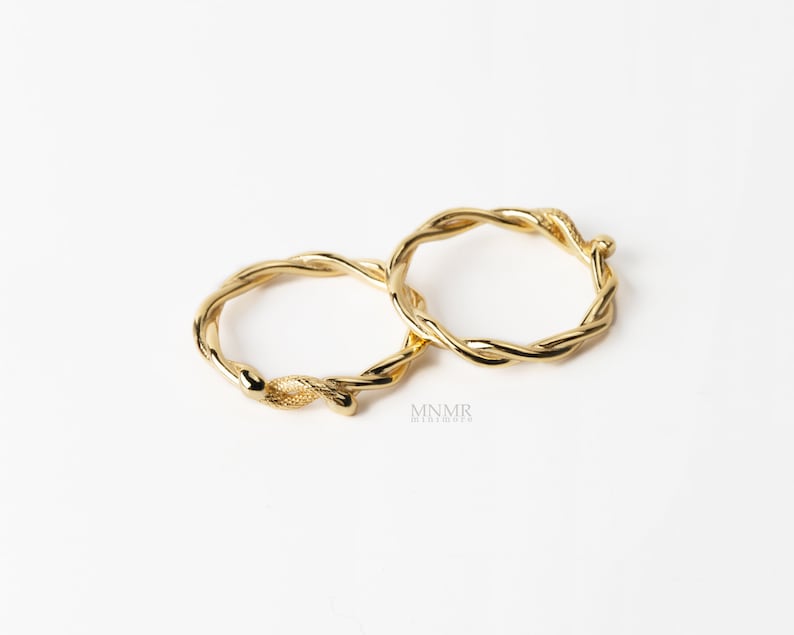 May include: Two gold-toned rings with a twisted, vine-like design. The rings are intertwined and appear to be made of metal.