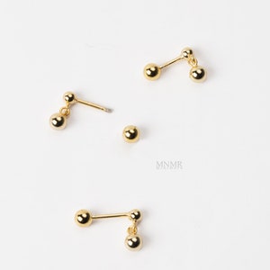 May include: Three pairs of gold-toned earrings with dangling ball charms. Each earring has two balls, one on the post and one dangling.