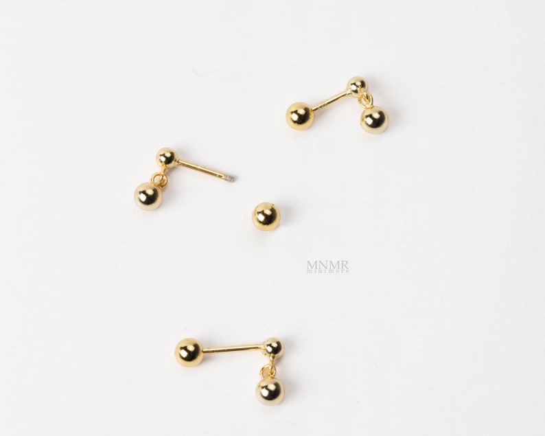 May include: Three pairs of gold-toned earrings with dangling ball charms. Each earring has two balls, one on the post and one dangling.