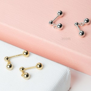 May include: Two pairs of earrings, one pair is gold and the other is silver. Both pairs have two small balls connected by a bar.
