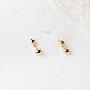 May include: A pair of gold dangle earrings with two round beads on each earring.