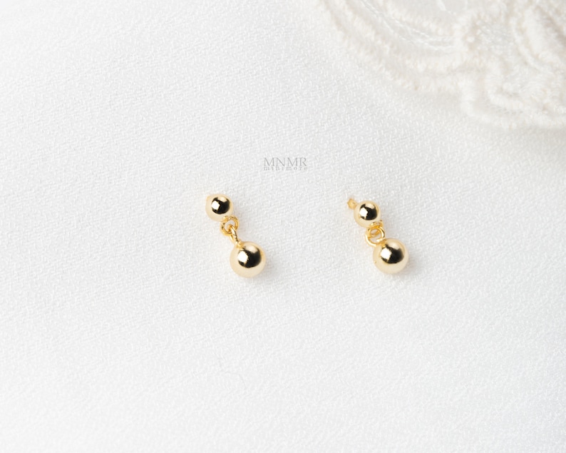 May include: A pair of gold dangle earrings with two round beads on each earring.