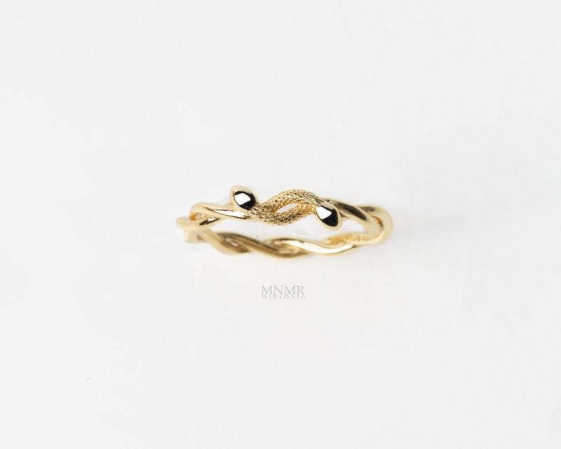 May include: A gold-toned ring with a twisted vine design. The ring features a textured surface and two small, rounded ends.