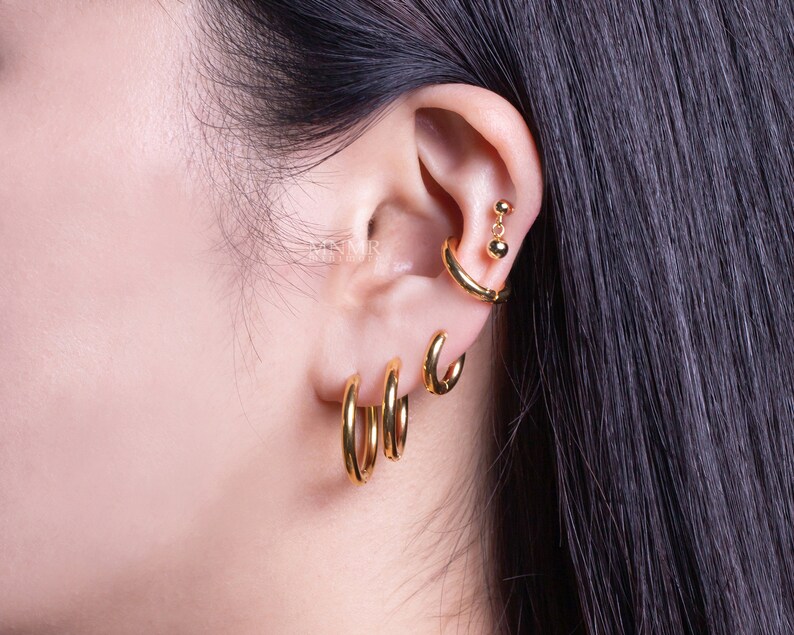May include: A person's ear with multiple gold hoop earrings. The earrings are different sizes and are worn in the lobe and cartilage.