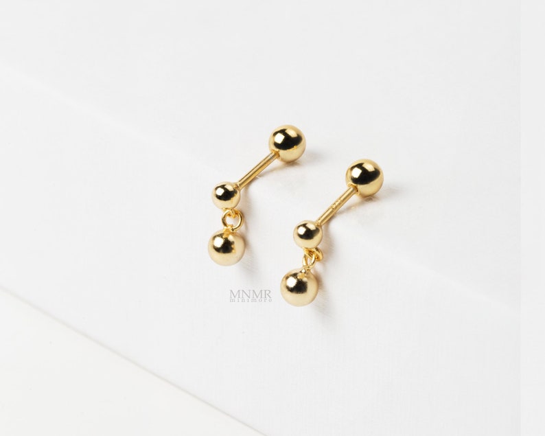 May include: A pair of gold dangle earrings with two small round balls on each earring.