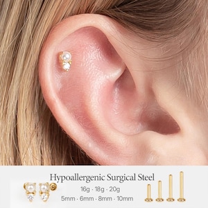 Könnte beinhalten: Ein goldfarbener Ohrstecker mit flacher Rückseite, einer kleinen weißen Perle und einem klaren runden Schmuckstein. Der Text Hypoallergenic Surgical Steel wird mit den Stärken 16g, 18g, 20g und Längen 5mm, 6mm, 8mm, 10mm sowie vier Metallstäben gezeigt.