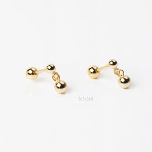 May include: A pair of gold dangle earrings with three small round balls on each earring.