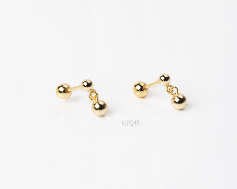 May include: A pair of gold dangle earrings with three small round balls on each earring.