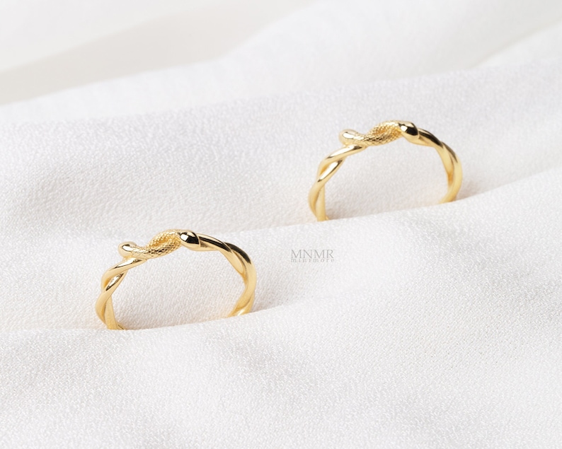 May include: Two gold-toned rings with a snake design. The rings are intertwined and have a smooth, polished finish.