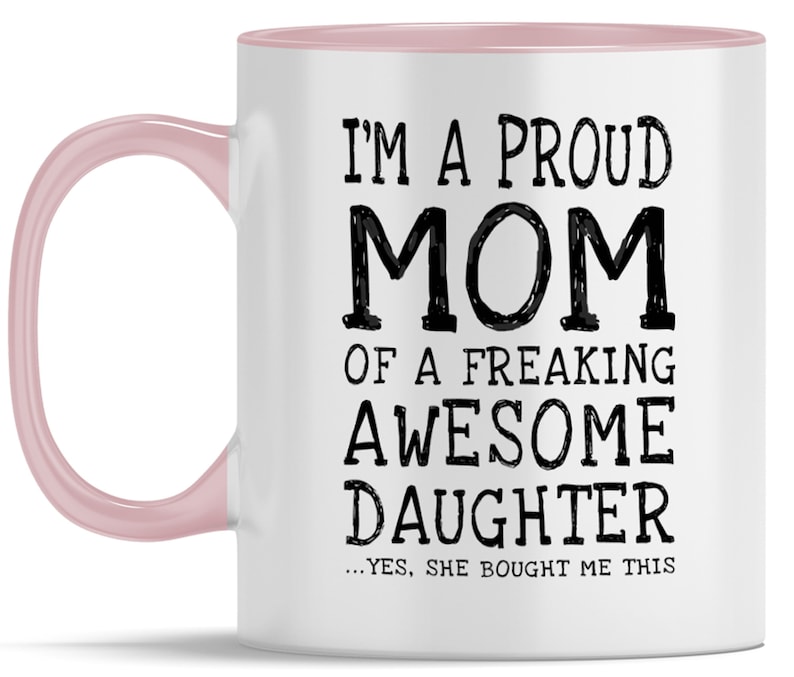 May include: White ceramic coffee mug with a pink rim and handle. The mug features black text that reads "I'm a proud mom of a freaking awesome daughter...yes, she bought me this."