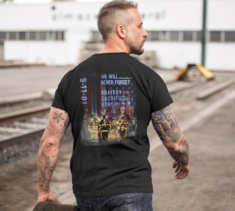 Pu&ograve; includere: Maglietta nera con una grafica di vigili del fuoco davanti a una bandiera americana. Il testo "We Will Never Forget" e "9-11-01" sono stampati sulla maglietta. La grafica include anche le parole "Bravery", "Sacrifice" e "Honor".