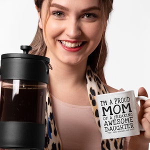 May include: White ceramic coffee mug with black text that reads "I'm a proud mom of a freaking awesome daughter...yes, she bought me this".