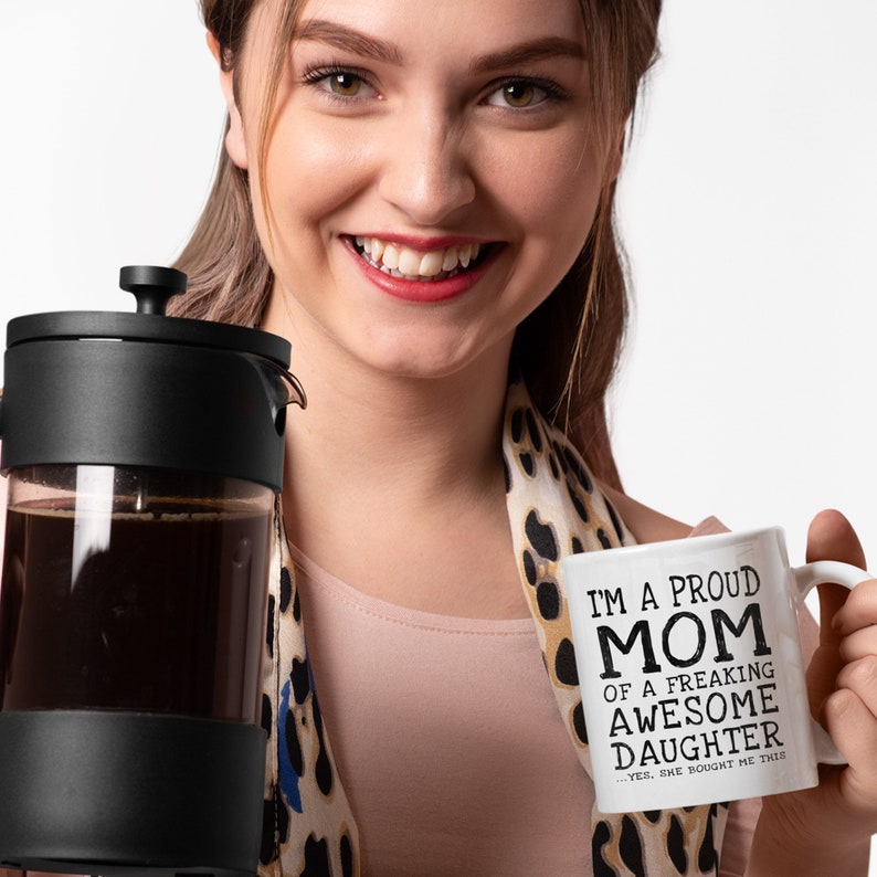 May include: White ceramic coffee mug with black text that reads "I'm a proud mom of a freaking awesome daughter...yes, she bought me this".