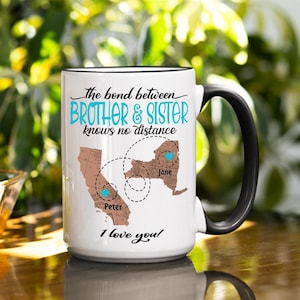 May include: White ceramic mug with a black handle and rim. The mug features the text "The bond between BROTHER & SISTER knows no distance" in black and teal. It also shows two state maps with names and hearts, and the words "I love you!"