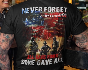 May include: Black t-shirt with a graphic of the American flag, firefighters, and the Twin Towers. The text "Never Forget 9-11-2001" and "All Gave Some Some Gave All" is printed on the shirt.