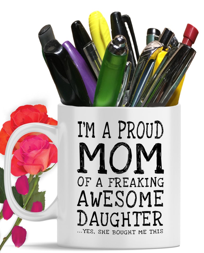 May include: White ceramic coffee mug with a black handle. The mug has black text that reads "I'm a proud mom of a freaking awesome daughter...yes, she bought me this".