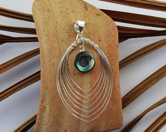 May include: A silver pendant with a round abalone shell inlay, surrounded by a delicate wire design. The pendant is on a brown textured surface.