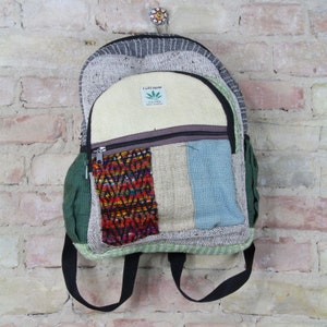 May include: A multi-colored hemp backpack with a green, blue, and white patchwork design. The backpack has a zippered pocket and a small green pocket on the side. The backpack has a label that says "Fair Hemp" with a green leaf logo and the text "The True Hemp Made in Nepal".