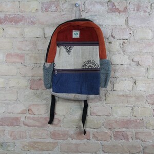 May include: A multi-colored hemp backpack with a brown, blue, and beige patchwork design. The backpack has a small green leaf logo with the text "Hempstory" on it.