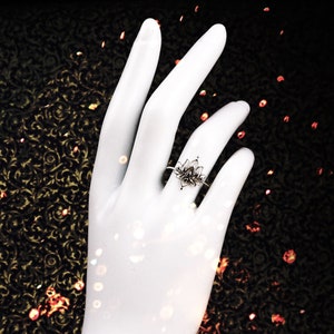 Puede incluir: Un anillo de plata con un dise&ntilde;o de flor de loto. El anillo est&aacute; en un dedo.