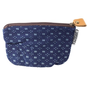 May include: A small blue zippered pouch with a white and blue patterned design. The pouch has a brown zipper and a brown leather pull tab with a metal ring. The pouch has a "FREAK SCENE" label on the side.