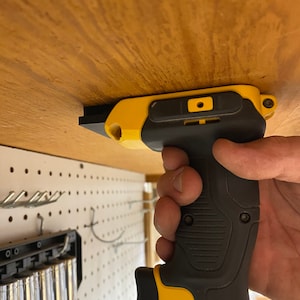 May include: A yellow and black cordless drill with a black handle and a yellow trigger. The drill is mounted to a wooden surface.