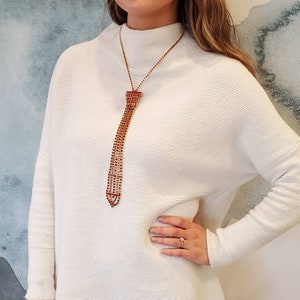 May include: A white sweater with a red rhinestone tie necklace. The necklace is made of small red rhinestones that are strung together to form a tie shape.