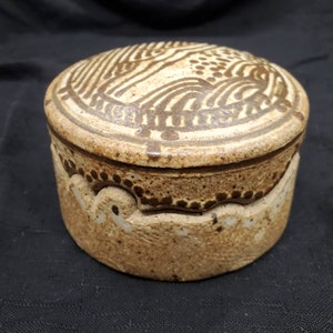 May include: A ceramic lidded jar with a brown and white geometric design. The jar has a rounded shape and a textured surface.